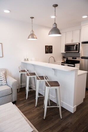 Una cucina moderna con isola centrale, sgabelli da bar, elettrodomestici in acciaio inossidabile e illuminazione a sospensione.
