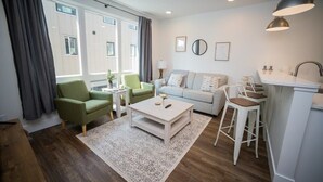A modern living room with a sofa, a coffee table, a green armchair, and a kitchen area with a bar stool. - Rooftop Condo in TC w/ Bay Views (Traverse City)