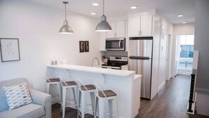 A modern kitchen with white cabinetry, stainless steel appliances, and a central island with bar stools. - Rooftop Condo in TC w/ Bay Views (Traverse City)