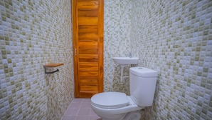 A bathroom with a tiled mosaic wall, a wooden door, a white toilet, and a small shelf. - Kos Bulan Bali (Tuban)