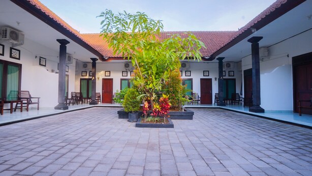 A courtyard with tiled flooring, potted plants, and traditional wooden doors. - Kos Bulan Bali (Tuban)