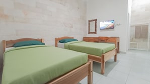 A room with two wooden beds with green bedding, a white brick wall, a television on the wall, and a white door. - Kos Bulan Bali (Tuban)