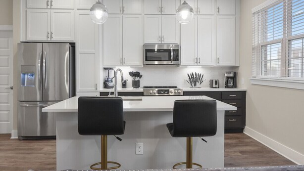 Una cocina moderna con armarios blancos, electrodomésticos de acero inoxidable e iluminación colgante.