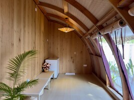 Un interior acogedor de madera, con un banco, una mesita con flores y un ventilador de techo.