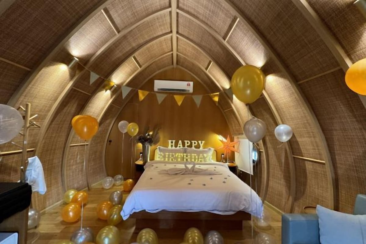 A cozy, arched-ceiling room with a bed, balloons, and a 'Happy Birthday' sign.