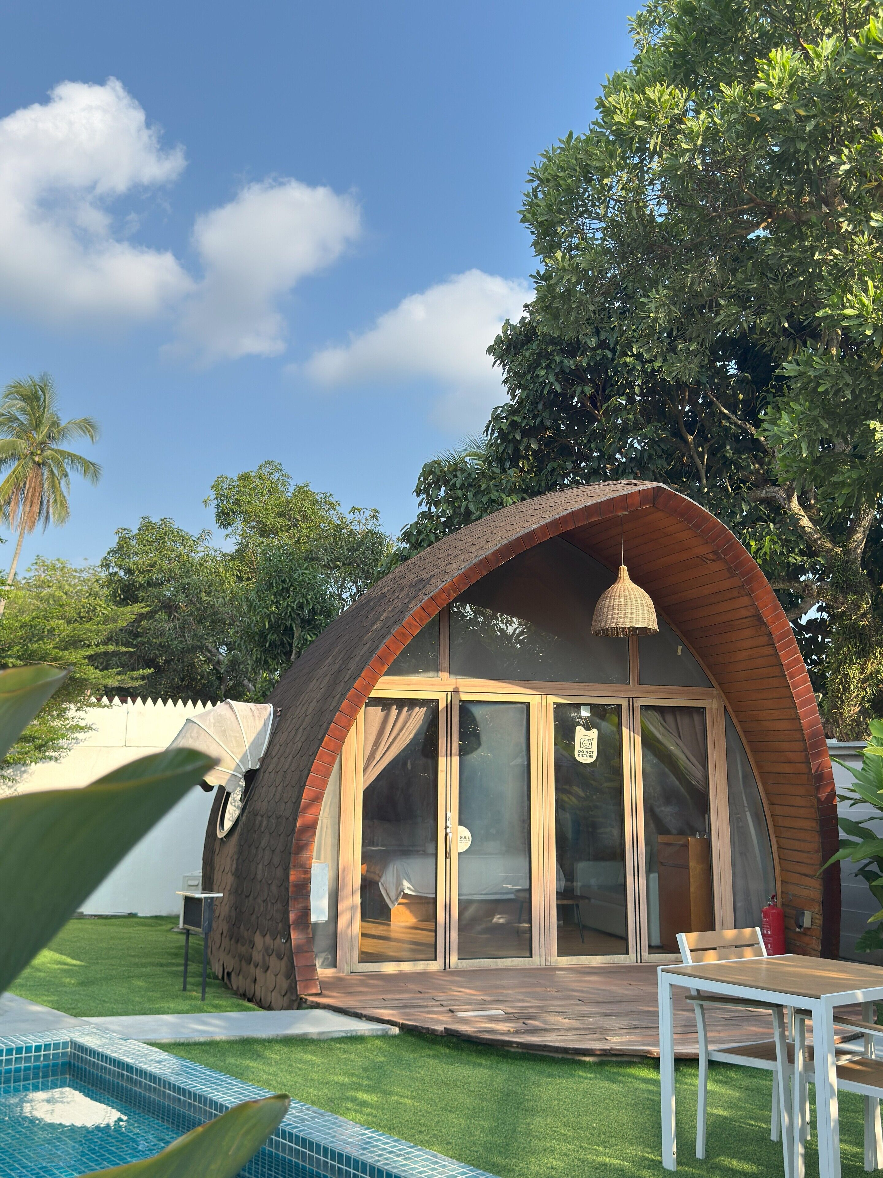 A dome-shaped building with a glass door and windows, surrounded by a pool and greenery.