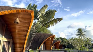 A row of wooden buildings with curved roofs, surrounded by tropical plants and palm trees. - Found Mansion Langkawi (Langkawi)
