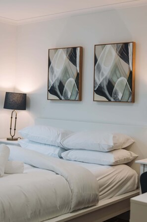 A hotel room with a bed, white bedding, a lamp, and two abstract paintings on the wall. - Lakeside 3-Bed Apartment with Jacuzzi (Belconnen)