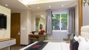 Een hotelkamer met een bed, een bureau, een spiegel, een raam met gordijnen en een televisie aan de muur.