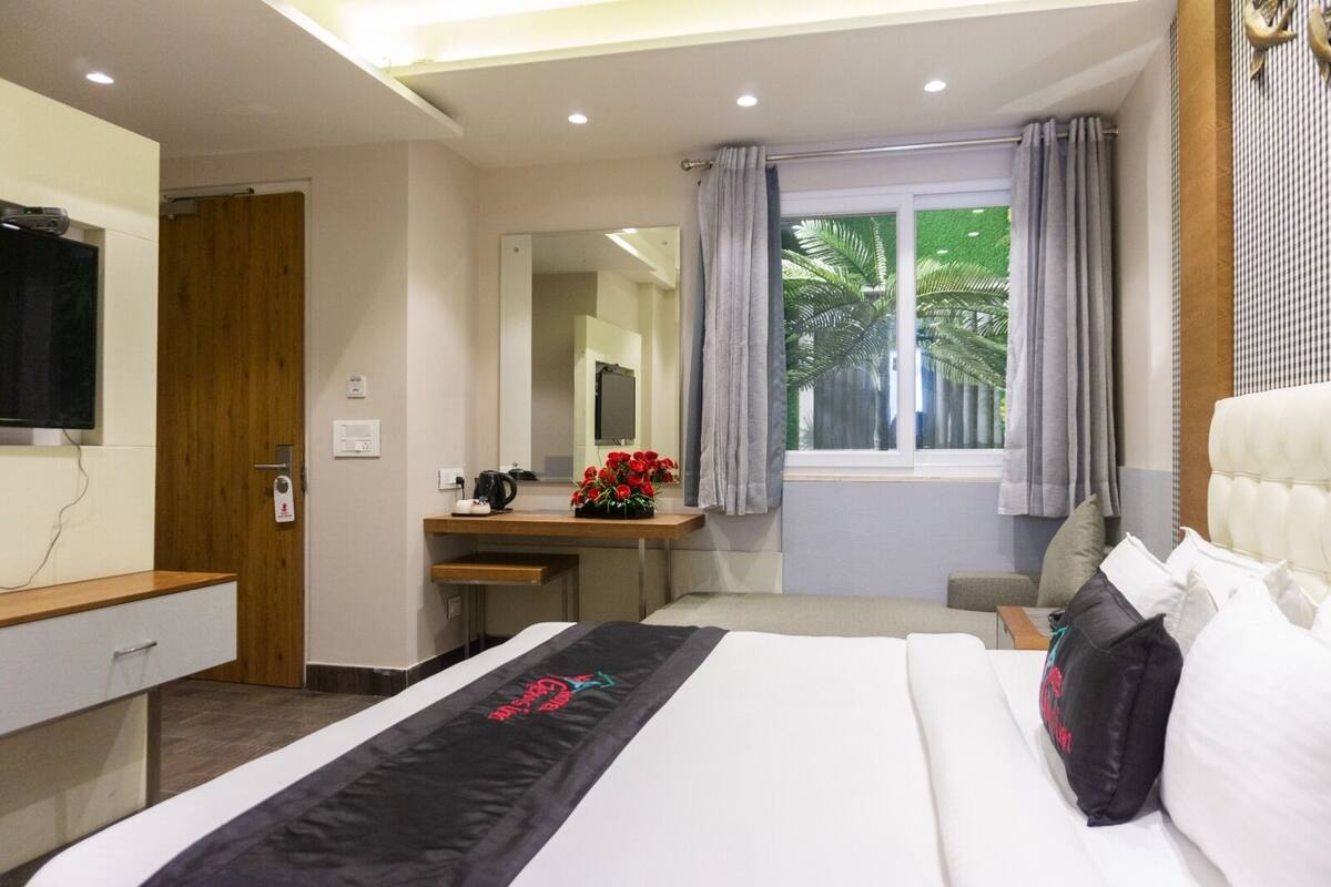 A hotel room with a bed, a desk, a mirror, a window with curtains, and a television on the wall.