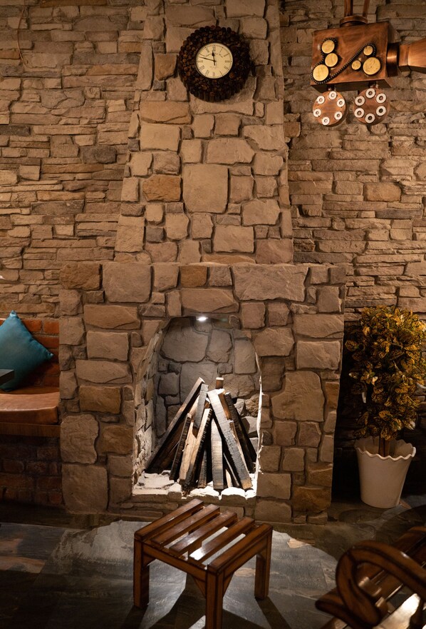 A stone fireplace with a mantel, a clock, and a decorative wooden piece. - Hotel Gems Inn (Vikasnagar)