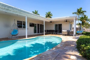 Uma piscina com área de estar, uma cadeira suspensa e um ventilador de teto.