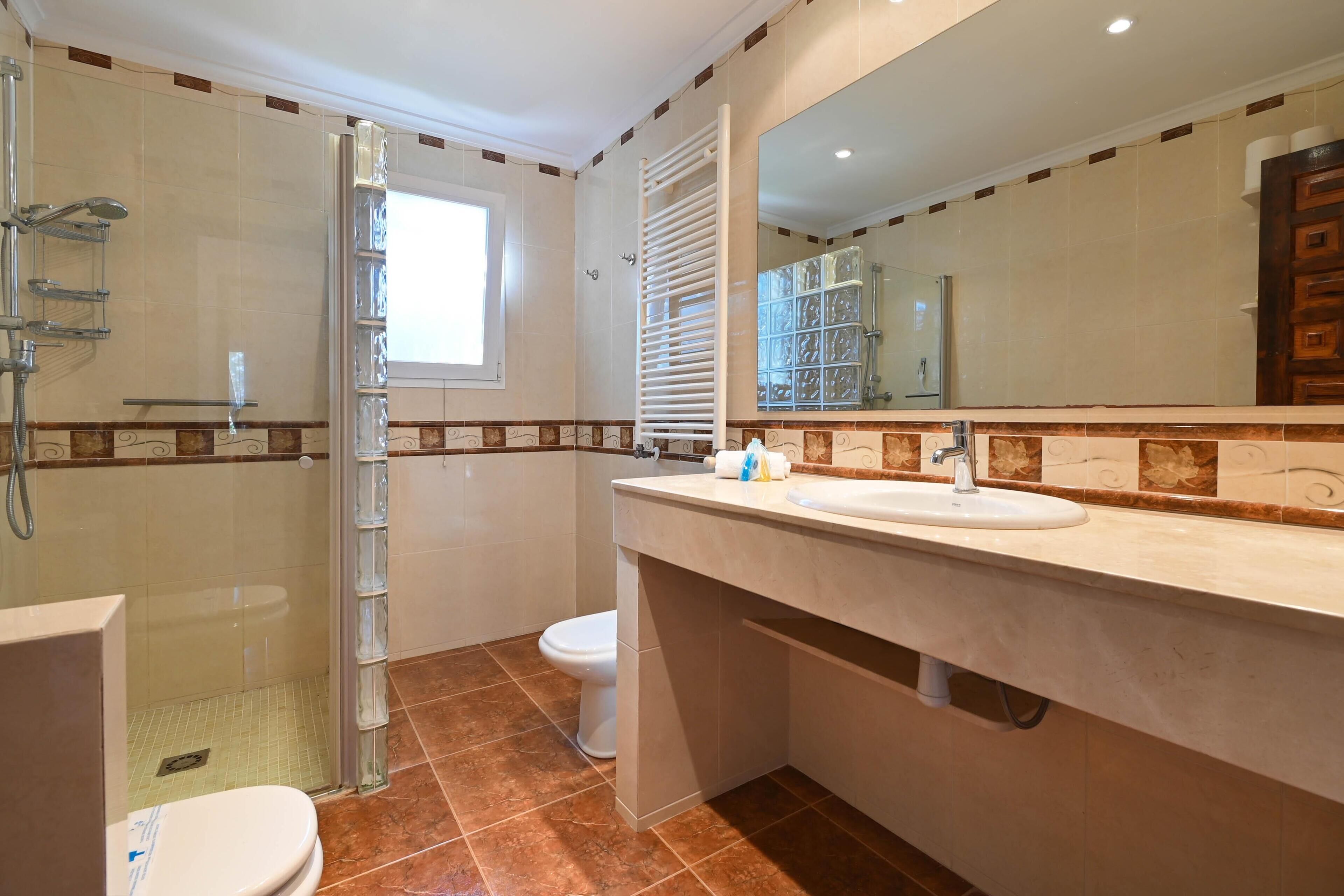 A bathroom with a glass-enclosed shower, a toilet, and a sink with a mirror above it.