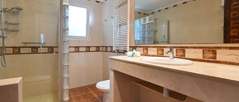 A bathroom with a glass-enclosed shower, a toilet, and a sink with a mirror above it.