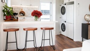 A modern kitchen with a central island, bar stools, a washing machine, and a globe on a cabinet. - Poolside Stay with City Views | Close to the Redwoods for Forest Adventures (Rotorua)