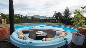 A backyard with a swimming pool, a covered seating area, and a brick wall. - Poolside Stay with City Views | Close to the Redwoods for Forest Adventures (Rotorua)