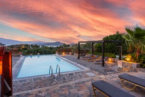A swimming pool with lounge chairs and a pergola, surrounded by stone flooring and greenery.