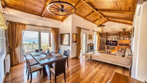 A spacious living room with a wooden ceiling, a dining area with a table and chairs, and a sofa. - Villa Glan Y Mor in Agios Nikolaos (Agios Nikolaos)