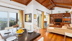 A spacious living area with a wooden ceiling, a dining table set with plates and glasses, a sofa, and a television. - Villa Glan Y Mor in Agios Nikolaos (Agios Nikolaos)
