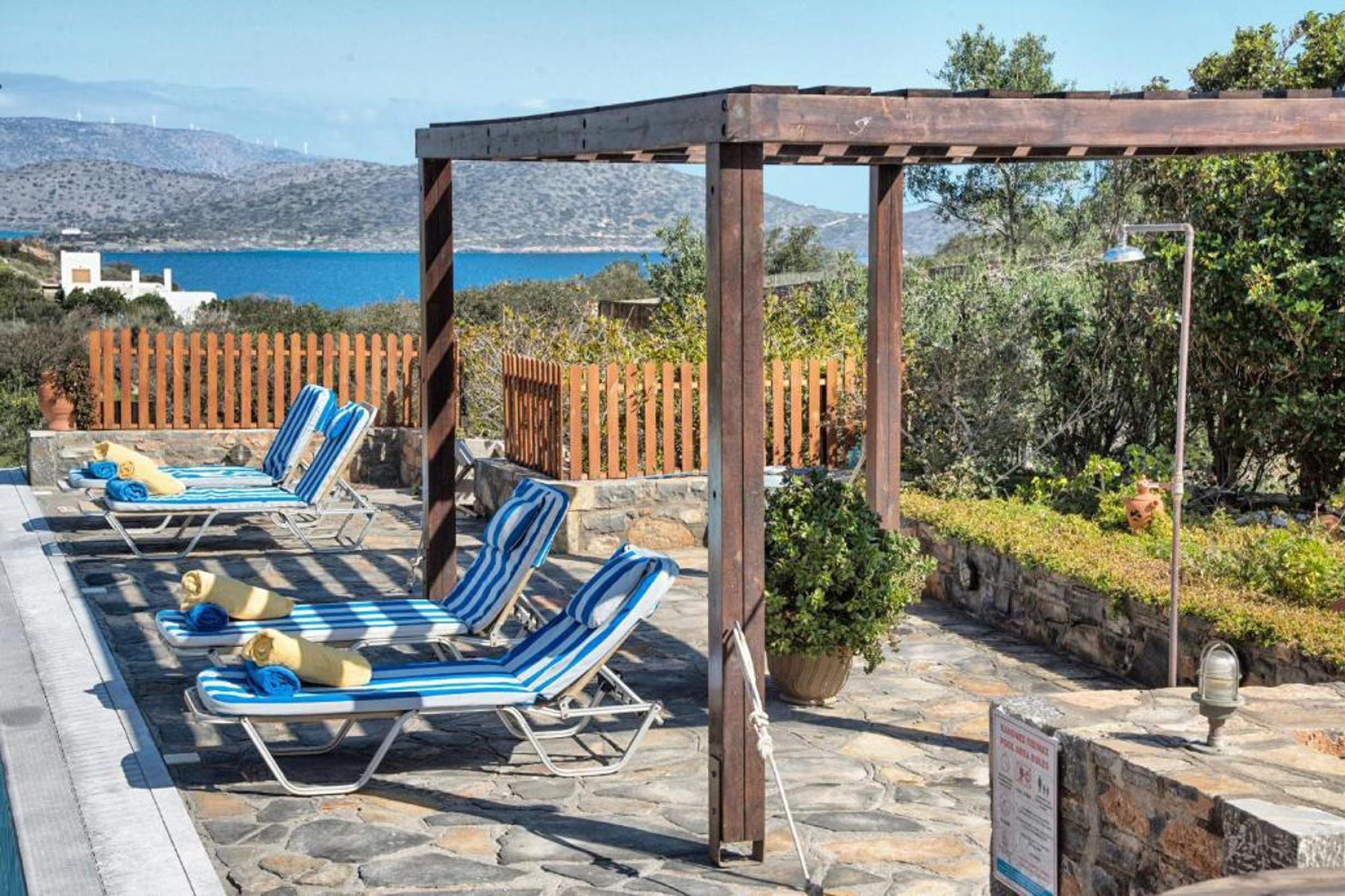 A poolside area with lounge chairs and a pergola, overlooking a body of water and hills.