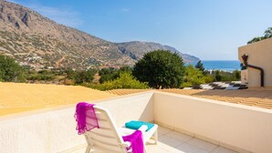 A balcony with a white chair and a blue cushion, overlooking a mountainous landscape and the sea. - Villa Elounda Plaka in Plaka (Agios Nikolaos)