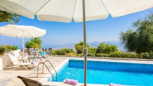 Un espace piscine agrémenté de chaises longues et de parasols, entouré de verdure et offrant une vue sur la mer.