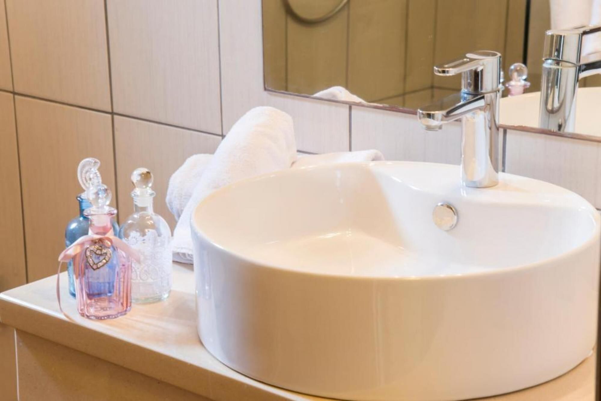 A white bathroom sink with a mirror above it, a towel, and two glass bottles with heart-shaped charms.