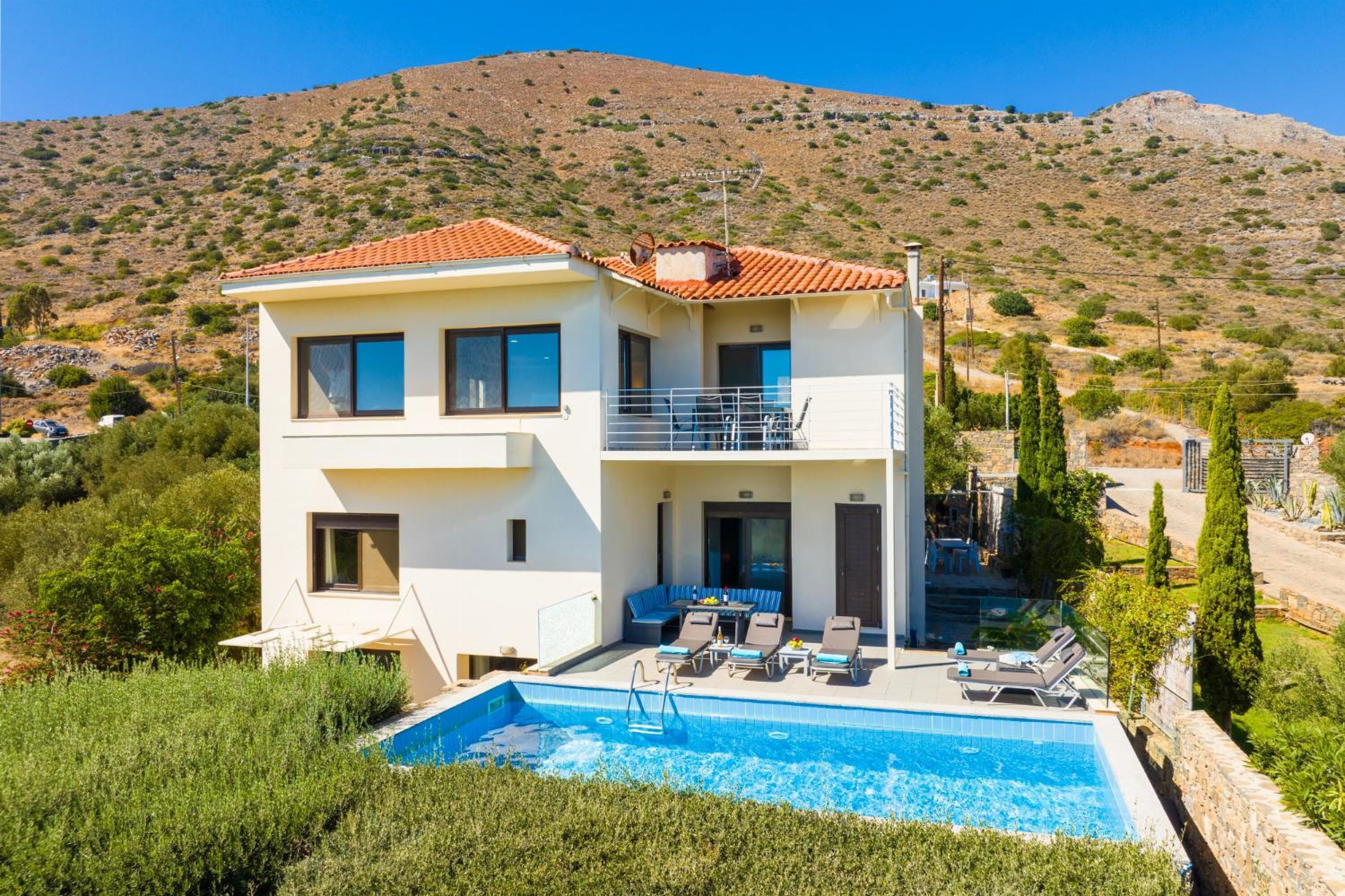 A two-story modern house with a swimming pool, a balcony, and a view of a hilly landscape.