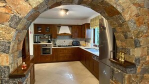 A kitchen with stone walls, wooden cabinets, a built-in oven, and a stainless steel refrigerator. - Villa Elounda Blue in Plaka (Agios Nikolaos)