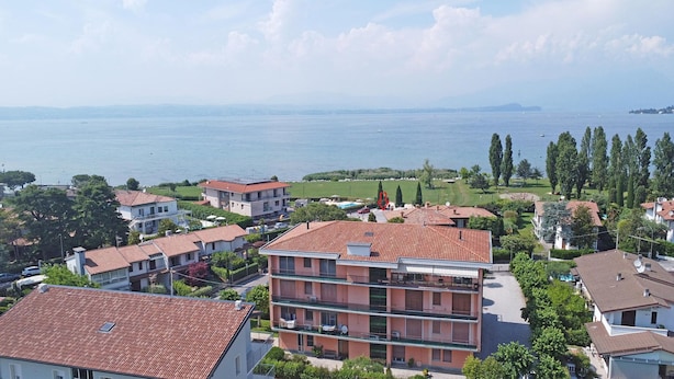 A coastal residential area with terracotta-roofed buildings, a view of the sea, and a park with a tennis court. - Appartamento Brema in Sirmione (Sirmione)