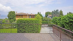 A residential area with a paved patio, a metal fence, and a view of houses and greenery. - Appartamento Brema in Sirmione (Sirmione)