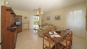 A spacious living area with a wooden dining table, a sofa, and a television. - Appartamento Brema in Sirmione (Sirmione)