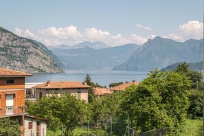 Ein Küstendorf mit Häusern mit Terrakotta-Dächern, einem See und Bergen im Hintergrund.