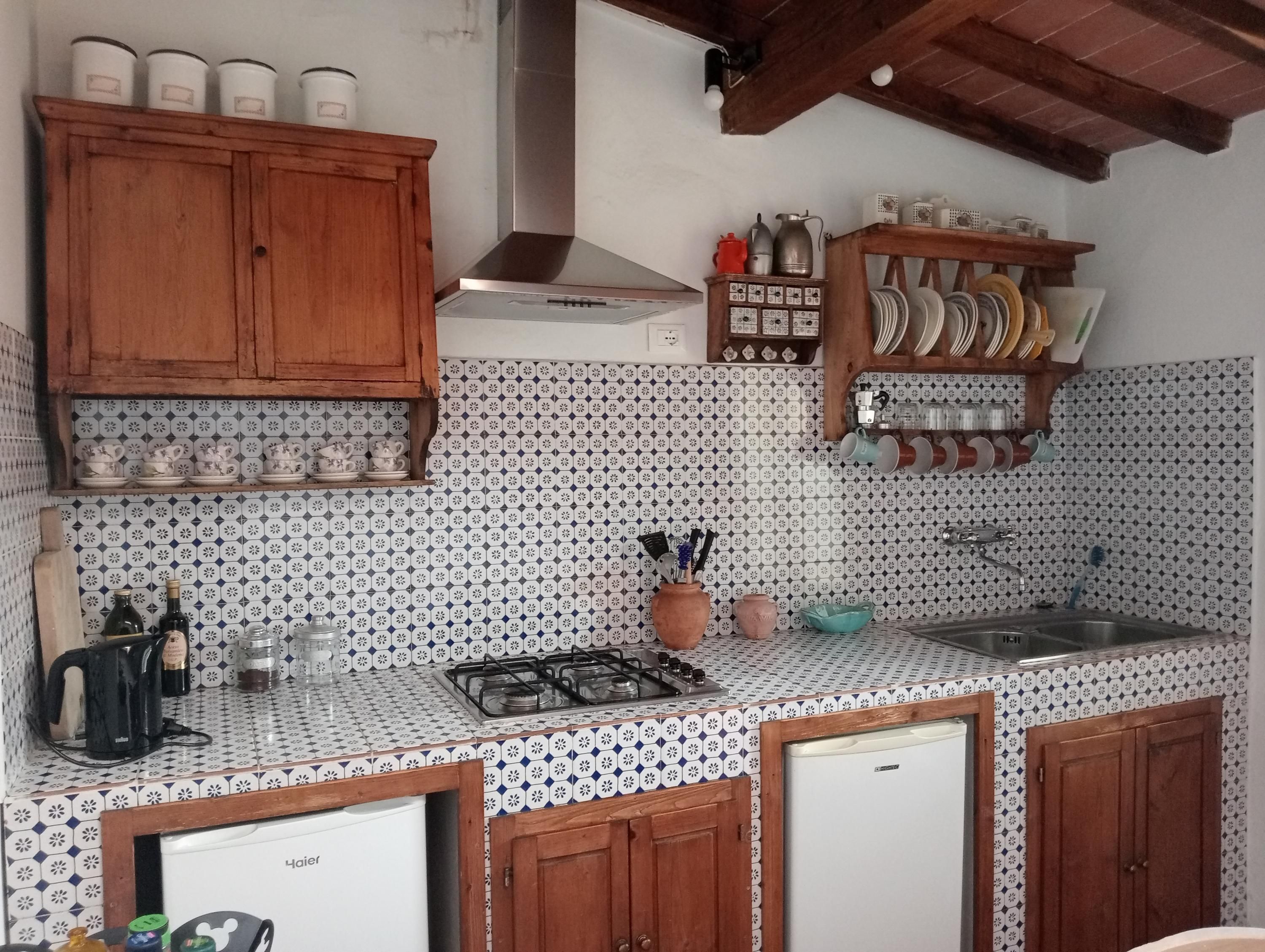 A kitchen with a tiled backsplash, wooden cabinets, a gas stove, a sink, and a refrigerator.