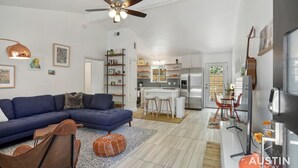 A modern living room with a blue sectional sofa, a ceiling fan, and a kitchen in the background. - Stylish Austin Retreat w/ Luxurious King Bed + W/D (Austin)