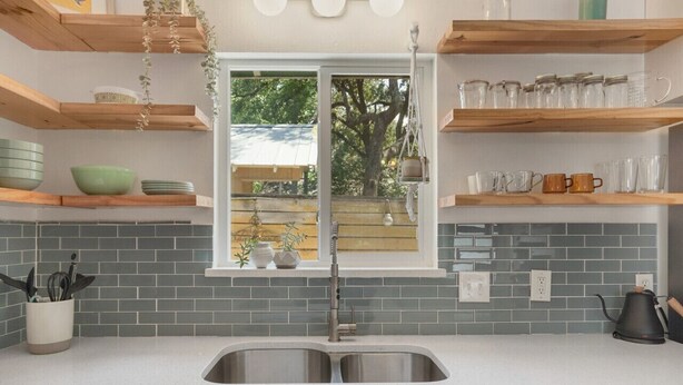 A kitchen with a double sink, wooden shelves, and a window with a view of trees. - Stylish Austin Retreat w/ Luxurious King Bed + W/D (Austin)