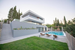 A modern two-story house with a swimming pool, outdoor seating, and a well-maintained lawn.