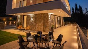 Une maison moderne à deux étages, dotée d’un espace repas extérieur circulaire et de murs en pierre.