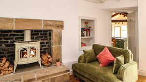 A cozy living room with a stone fireplace, a green sofa with a red pillow, and a wooden floor. - Old Wool Shop (Leyburn)