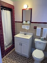 Un baño con ducha, lavamanos, inodoro y espejo.