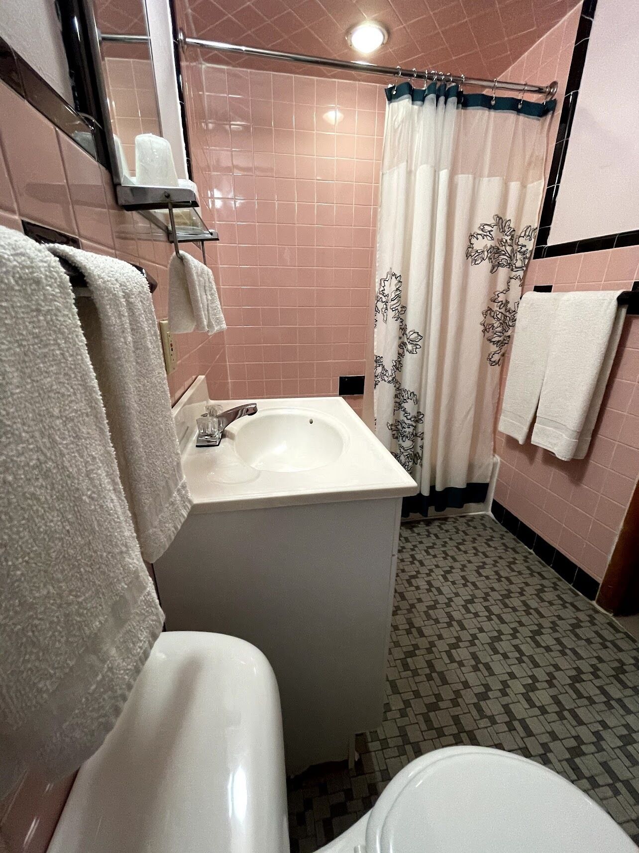 A bathroom with a white sink, a toilet, a shower curtain with a floral pattern, and pink tiled walls.