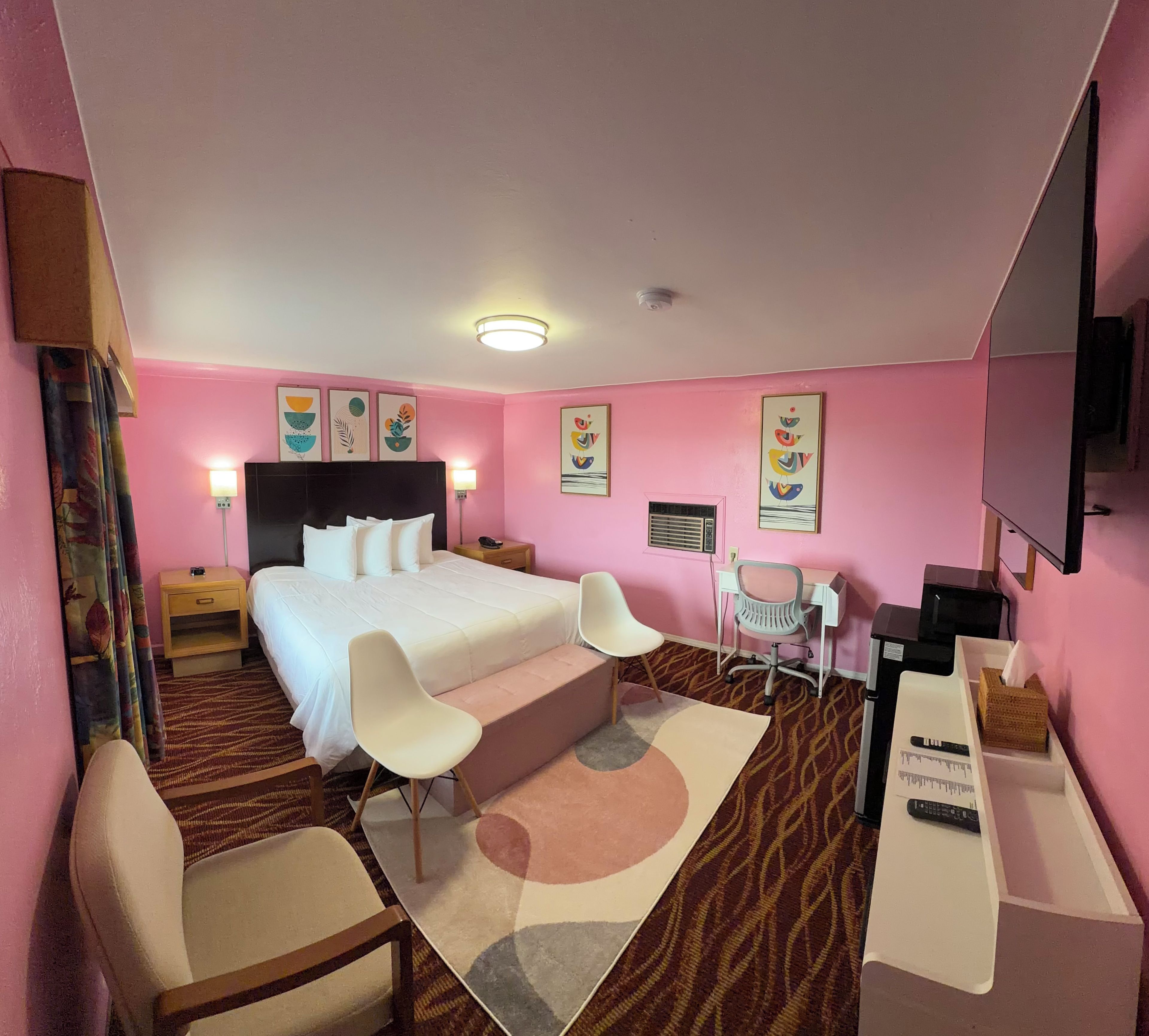 A hotel room with a bed, two chairs, a desk, and a TV.