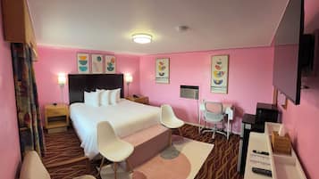 A hotel room with a bed, two chairs, a desk, and a TV.
