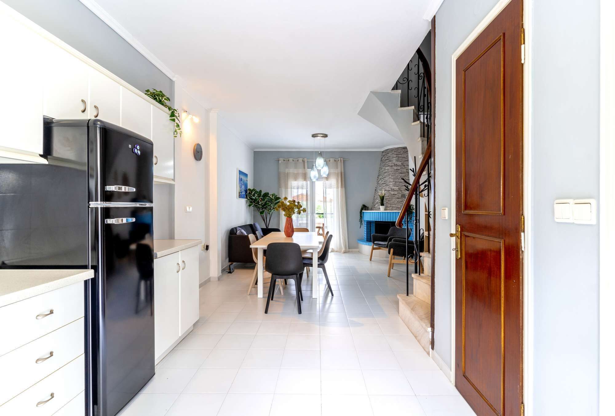 Une cuisine moderne avec des meubles blancs, un réfrigérateur noir et un coin repas comprenant une table et des chaises.