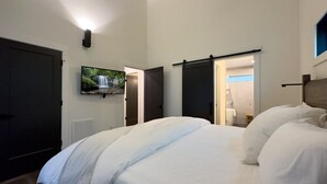 Ein Hotelzimmer mit Bett, Fernseher, einer Schiebetür und einem durch eine offene Tür einsehbaren Badezimmer.