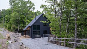 Eine moderne Holzhütte namens Hemlock Cottage mit einer Schotterauffahrt und einem Holzzaun.