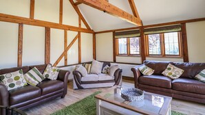 A spacious living room with exposed wooden beams, two leather sofas with patterned cushions, a glass coffee table, and a large window providing natural light. - Awelfan (Newtown)