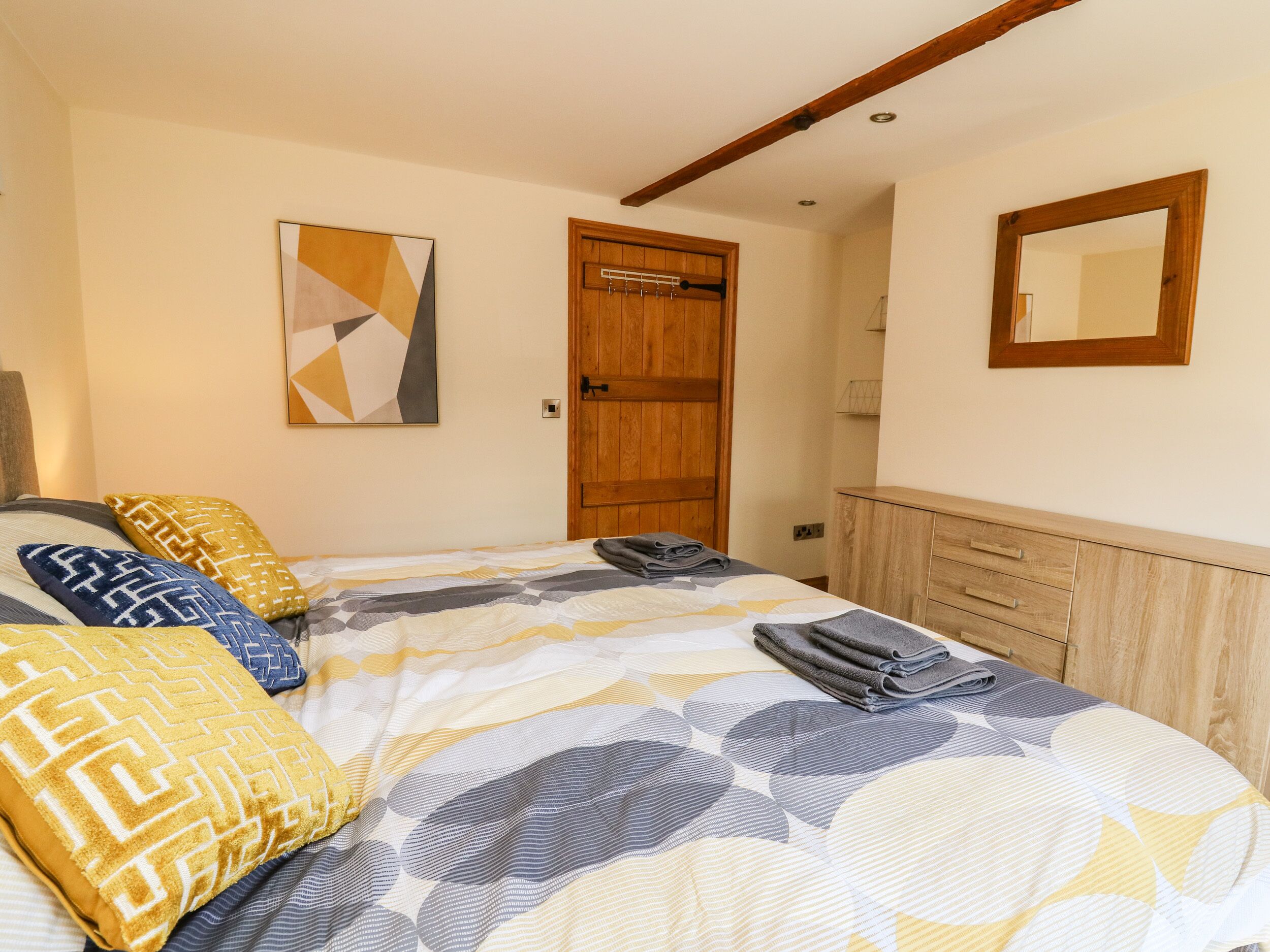 A bedroom with a bed, pillows, a wooden door, a mirror, and a wall-mounted artwork.