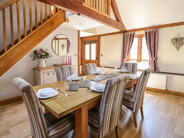 Comedor con una mesa de madera dispuesta para seis comensales, sillas a rayas, una escalera de madera y un espejo en la pared.
