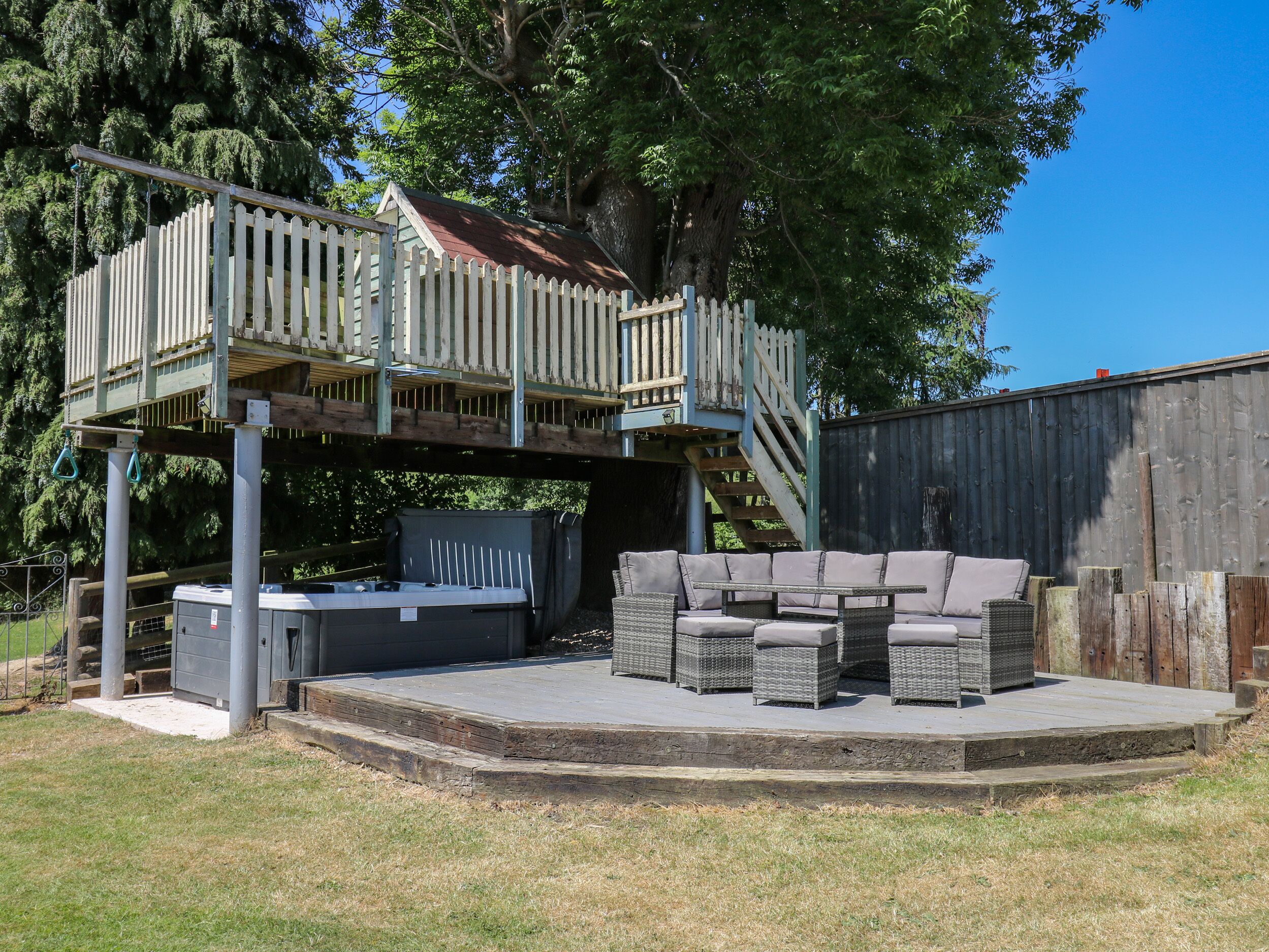 Eine Terrasse mit Gartenmöbeln, einem Whirlpool und einem überdachten Bereich mit Holzgeländer.